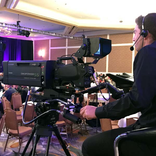 Camera operator with a box lens filming a conference
